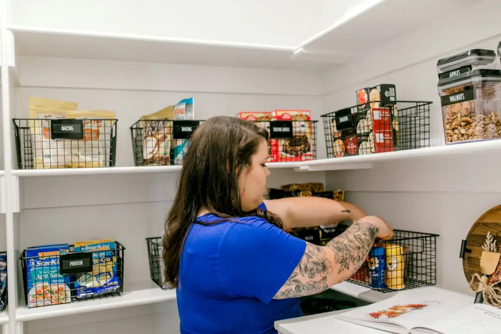 Woman arranging groceries into baskets on pantry shelves, illustrating meal planning and pantry